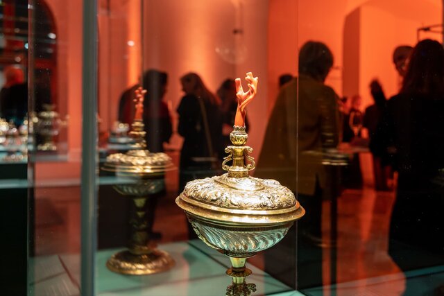 Im Vordergrund ist ein Kunststück in einer Vitrine erkennbar, im Hintergrund unterhalten sich mehrere Personen miteinanderIm Vordergrund ist ein Kunststück in einer Vitrine erkennbar, im Hintergrund unterhalten sich mehrere Personen miteinander