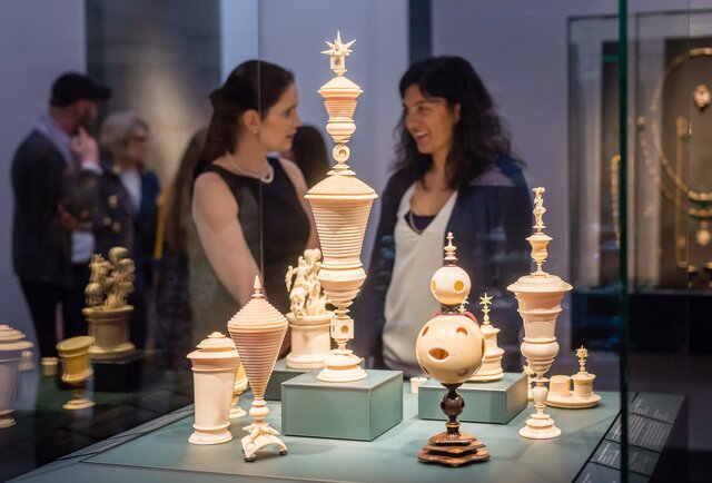 Im Vordergrund sind Ausstellungsstücke aus Elfenbern erkennbar, im Hintergrund zwei Frauen.